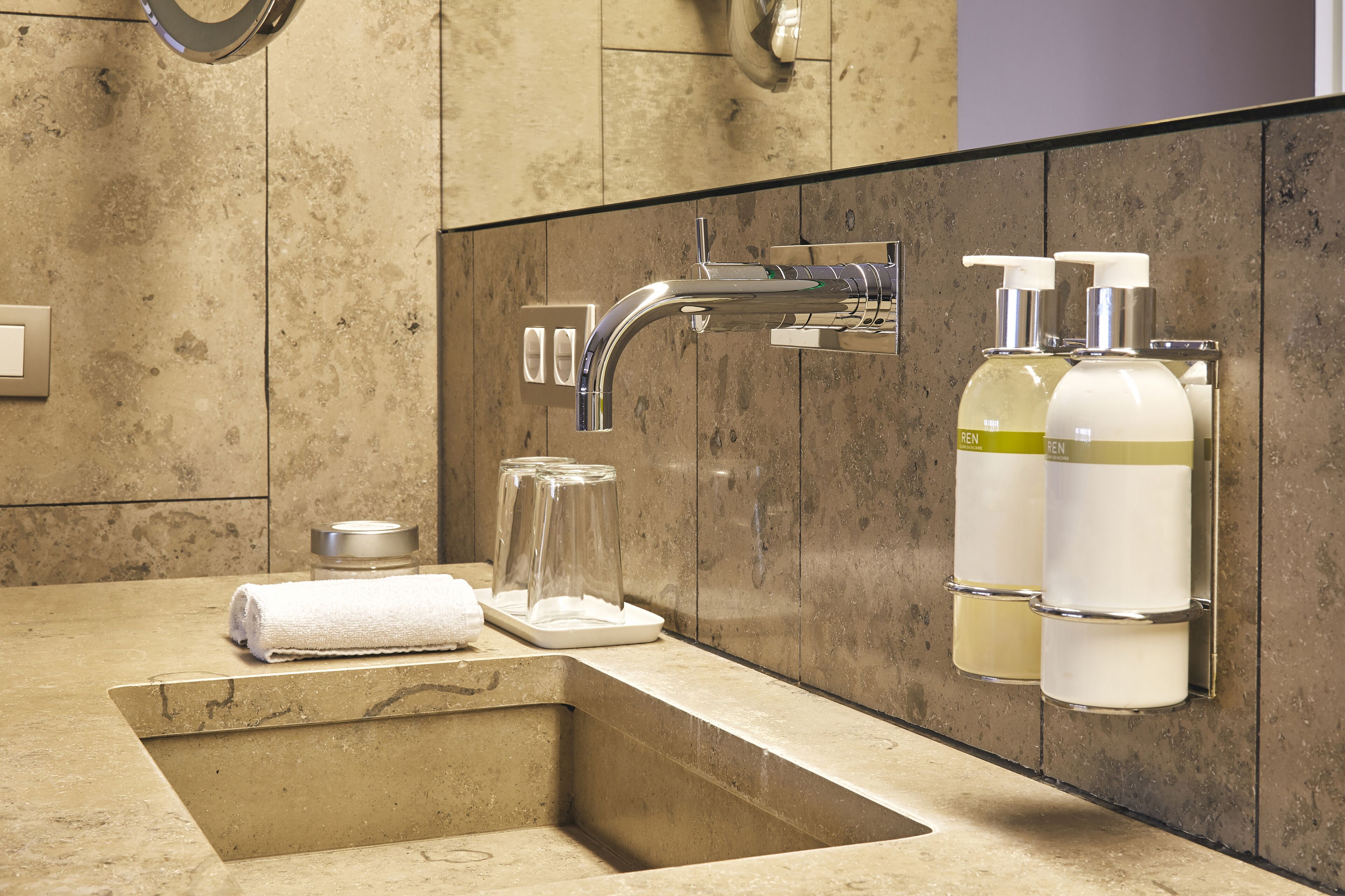 A bathroom with a marble sink, a modern faucet, and two hand sanitizer dispensers.