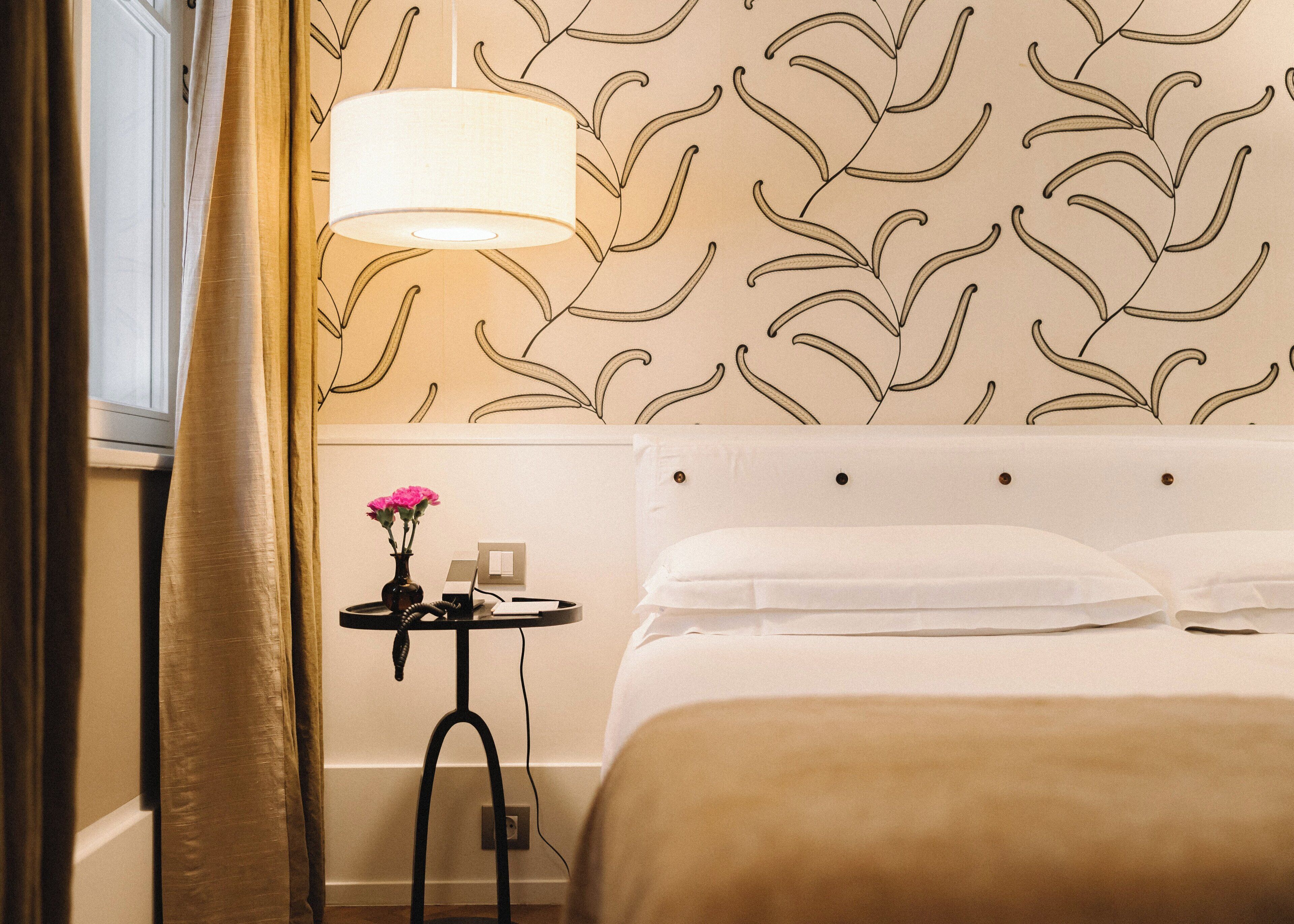 A hotel room with a bed, a bedside table with a lamp, and a wall with a leaf pattern.