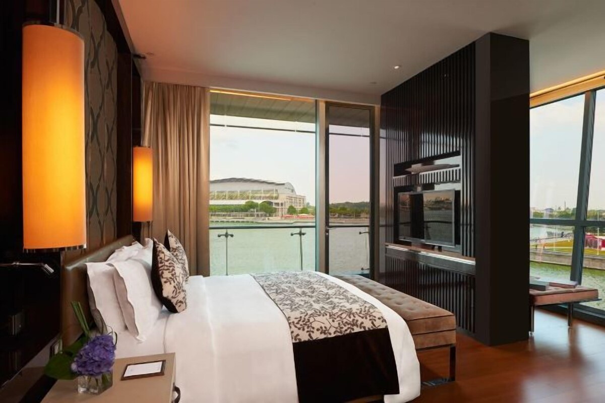 Habitación de hotel moderna con una cama grande, televisión y balcón con vistas a un edificio y al agua.
