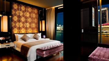 A modern hotel room with a large bed, a bench, and a view of a cityscape at night.
