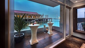 Een modern balkon met twee witte tafels, een bloempot en uitzicht op een gebouw aan de overkant van het water.