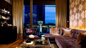 A modern living room with a city view, a plush sofa, a coffee table, and a bookshelf.