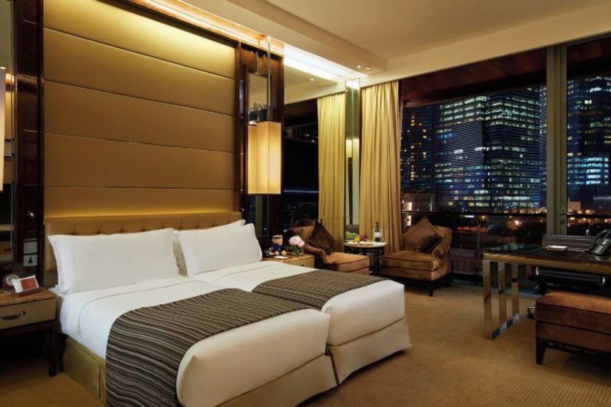 Habitación de hotel con una cama grande, un escritorio, una silla y vistas a la ciudad iluminada por la noche.