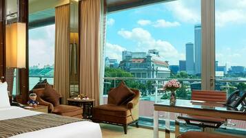 A hotel room with a large bed, two armchairs, a small table, and a view of the cityscape.