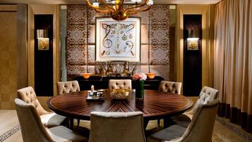 A formal dining room with a round table, six upholstered chairs, a chandelier, and patterned wallpaper.