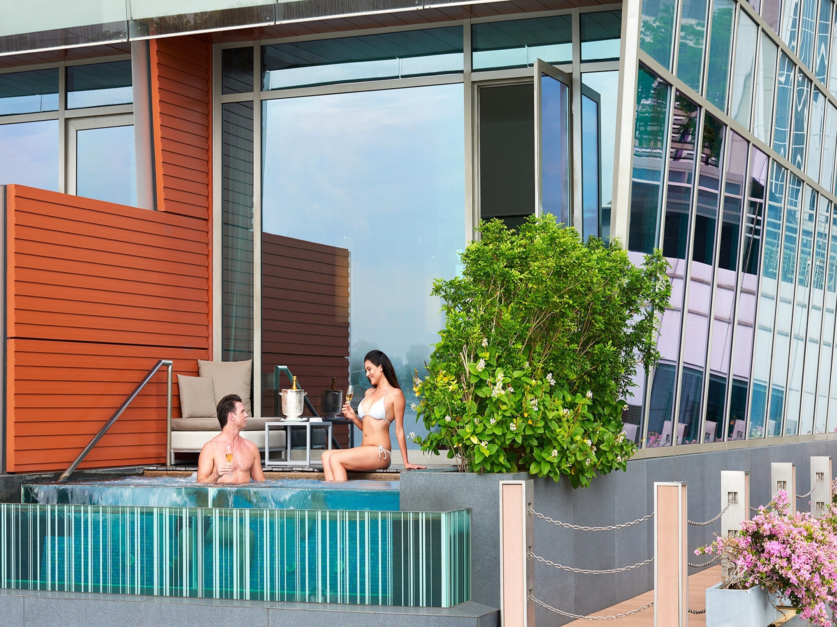 Un hotel moderno con zona de piscina, terraza de madera y fachada de cristal.