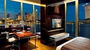 A modern hotel room with a large window overlooking a city skyline and a waterfront.