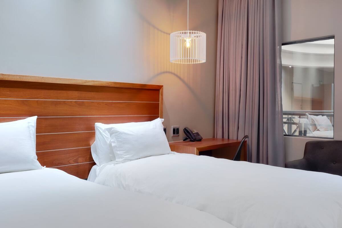 Une chambre d’hôtel avec une tête de lit en bois, un lit avec du linge de lit blanc, une table de chevet avec un téléphone et un luminaire suspendu.