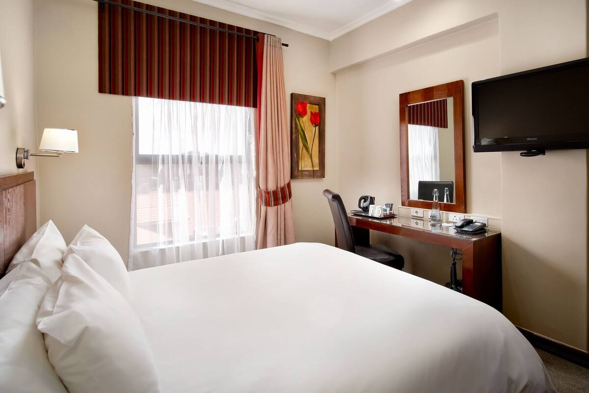 Une chambre d’hôtel avec un grand lit, un bureau avec un téléphone et un téléviseur.