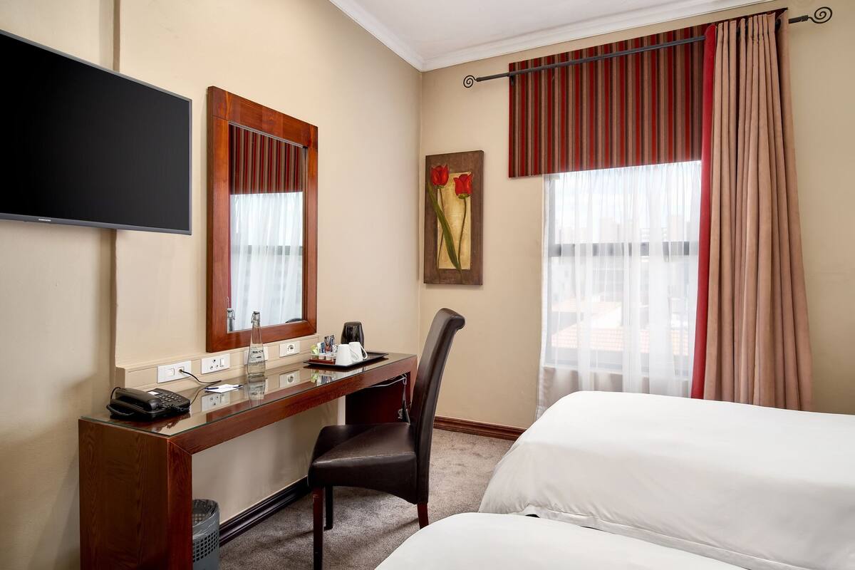 Une chambre d’hôtel comprenant un lit, un bureau avec un téléphone, une chaise, un téléviseur et une fenêtre avec des rideaux.