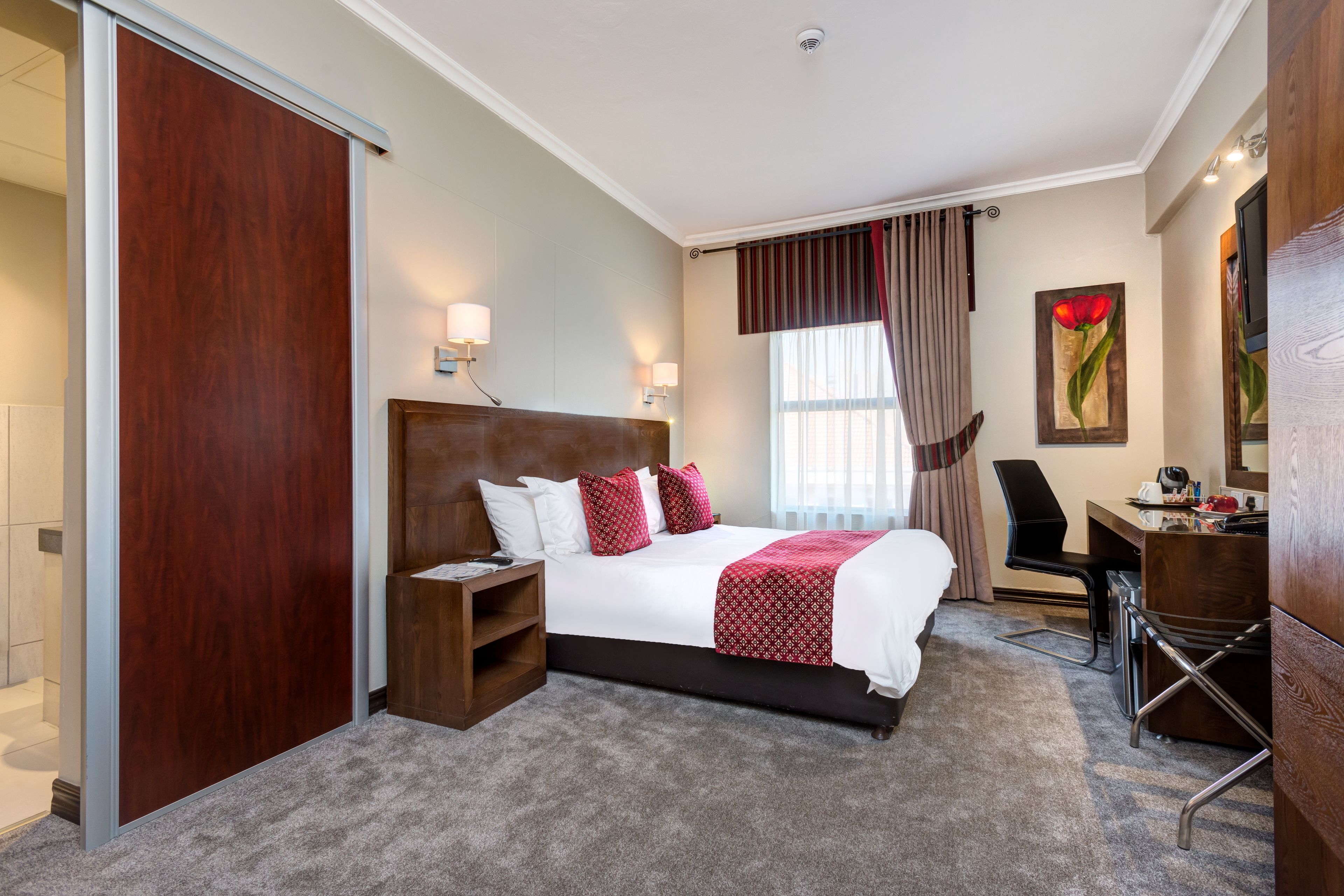 A hotel room with a large bed, a desk, a chair, a nightstand, and a wardrobe.