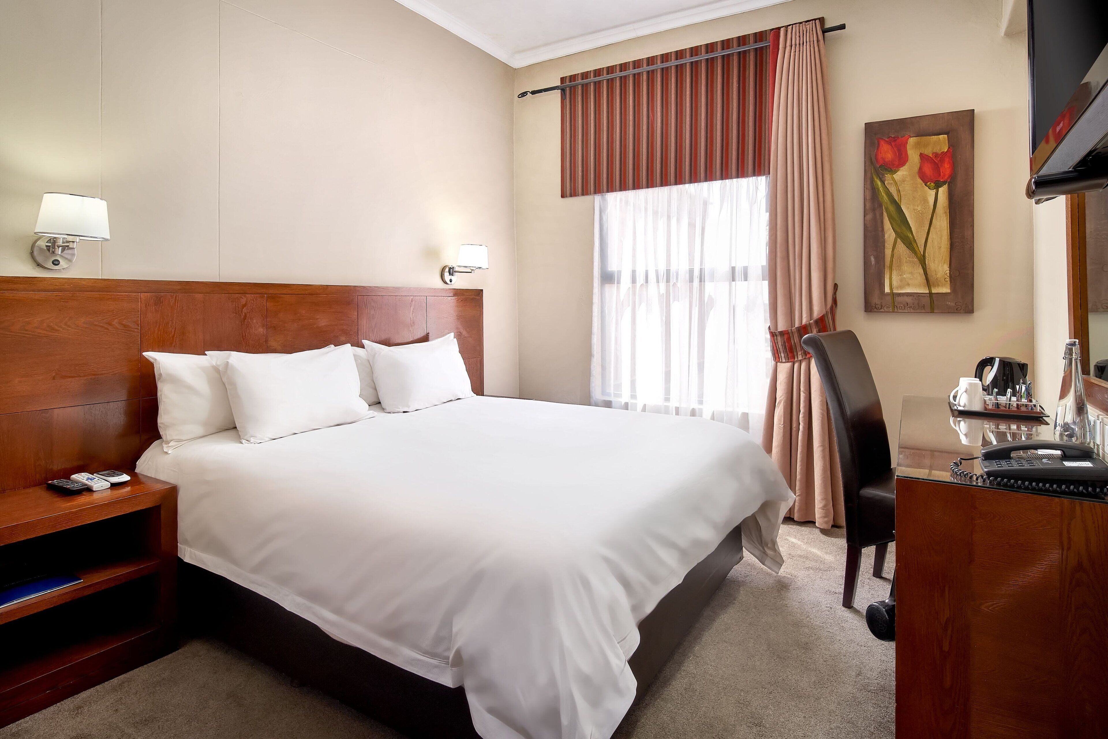 Una habitación de hotel con una cama grande, mesitas de noche, un escritorio con teléfono y una silla.
