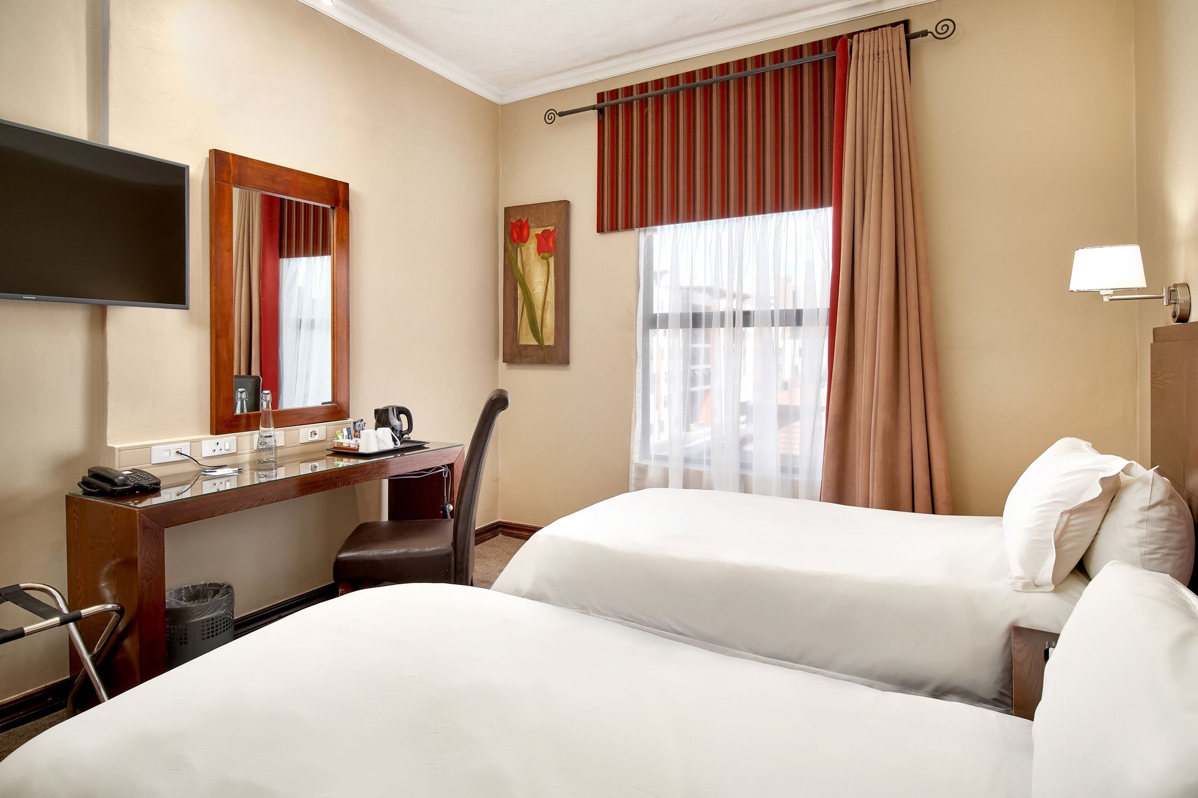 Ein Hotelzimmer mit zwei Betten, einem Schreibtisch mit Telefon, einem Fernseher und einem Fenster mit Vorhängen.