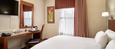 Une chambre d’hôtel comprenant un lit, un bureau avec un téléphone, une chaise, un téléviseur et une fenêtre avec des rideaux.