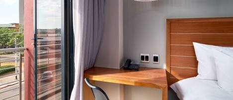 Habitación de hotel con cama, escritorio, teléfono, lámpara, y vista al exterior.