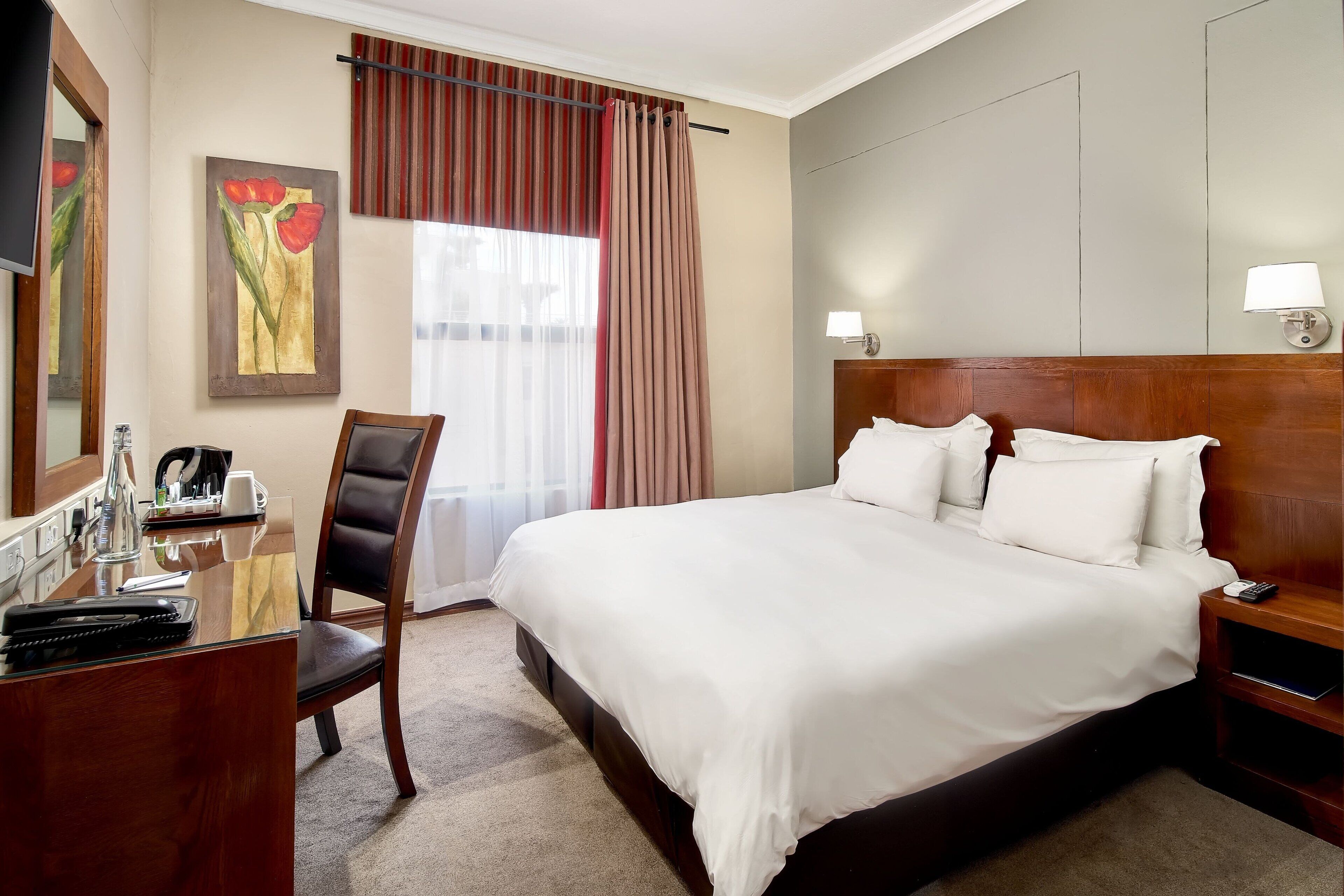 Habitación de hotel con una cama grande, un escritorio con silla, un teléfono y una lámpara en la mesita de noche.