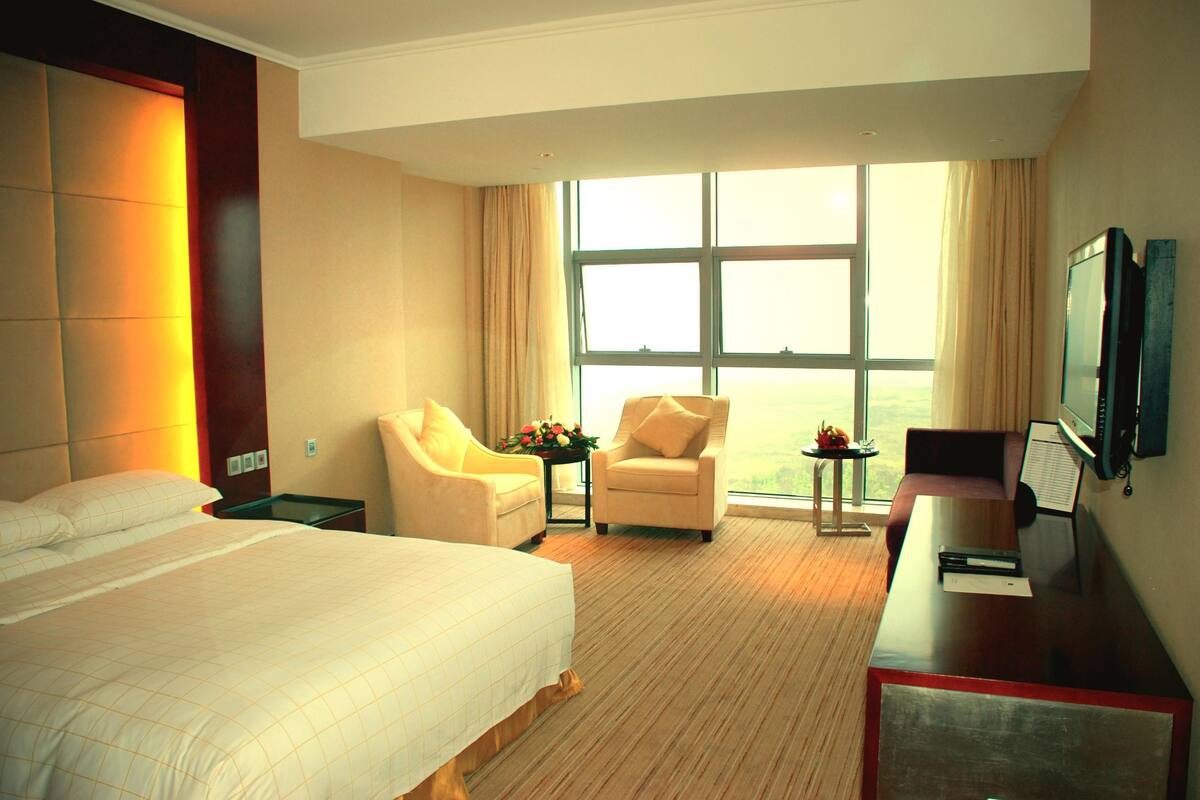 A hotel room with a large bed, two armchairs, a desk, and a TV.