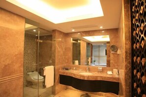 A modern bathroom with a glass shower enclosure, a vanity with a mirror, and a dark-colored sink. - Grand Metropark Hotel Chongqing (Chongqing)