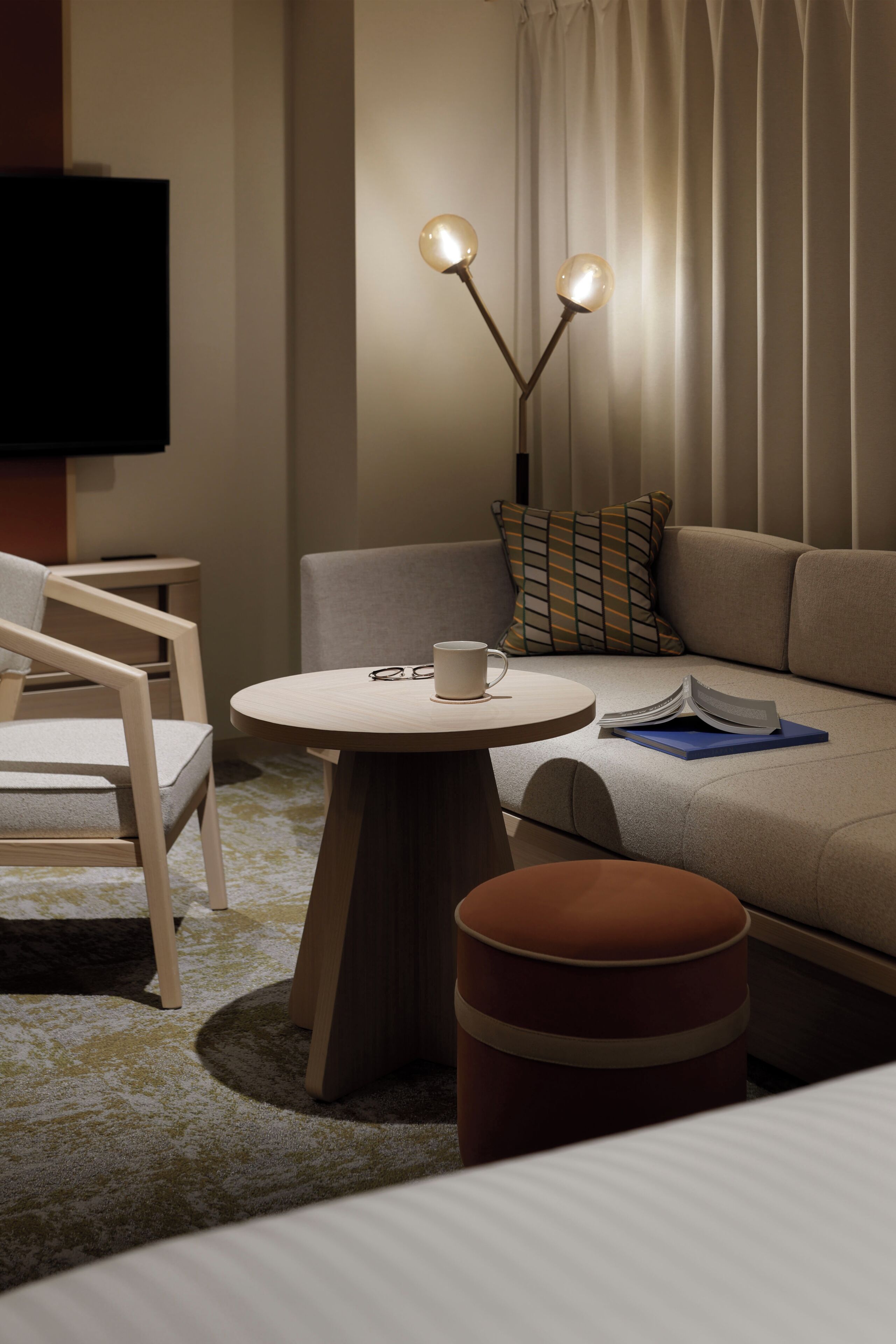 A modern hotel room with a round wooden table, a sofa, a TV, and a floor lamp.