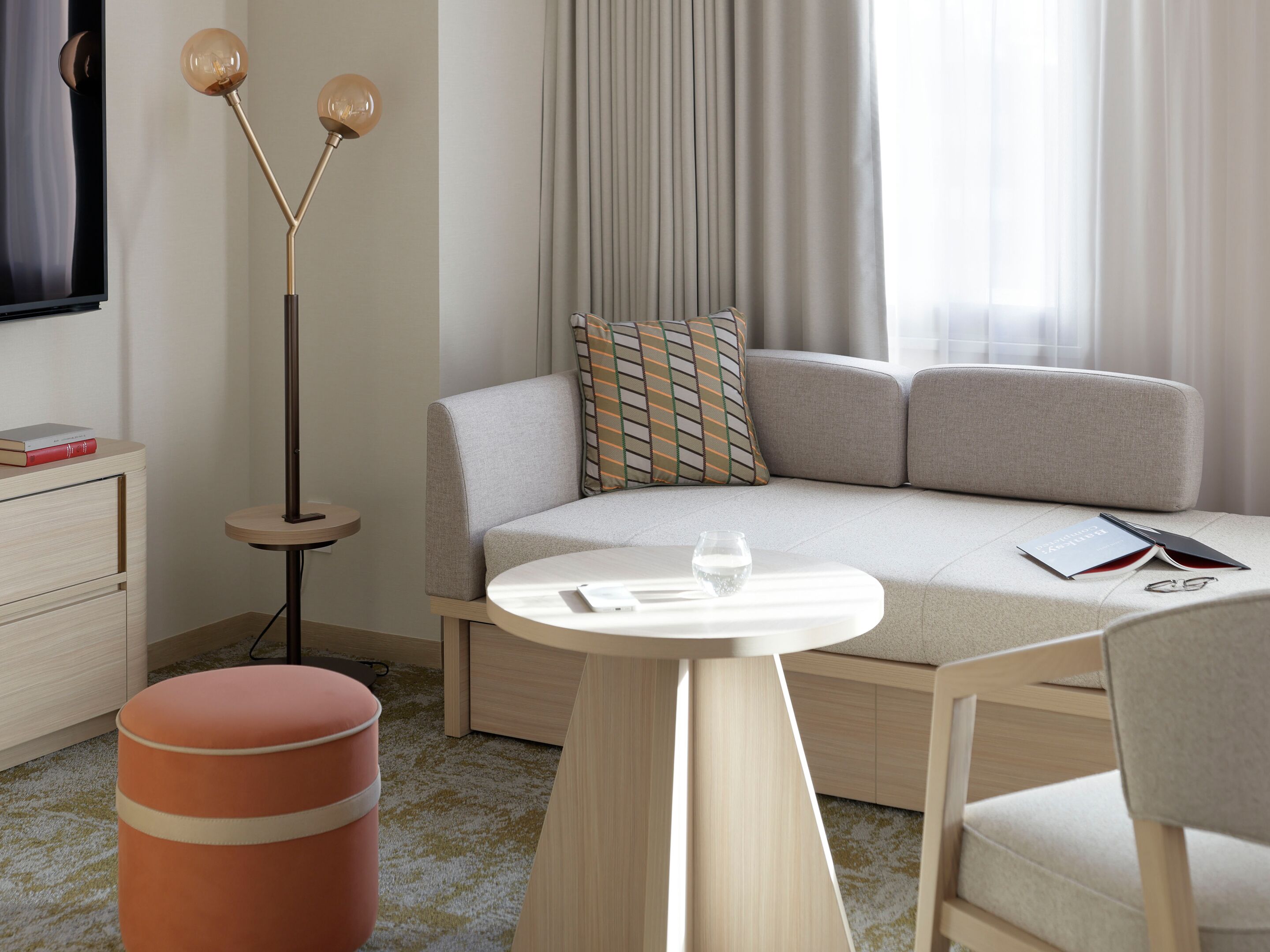 A modern hotel room with a sofa, a small round table, a floor lamp, and a trash bin.