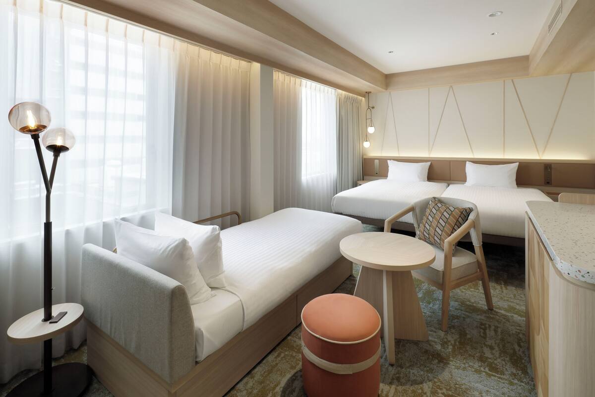 Quarto de hotel com cama, sofá, mesa pequena, cadeira e abajur.