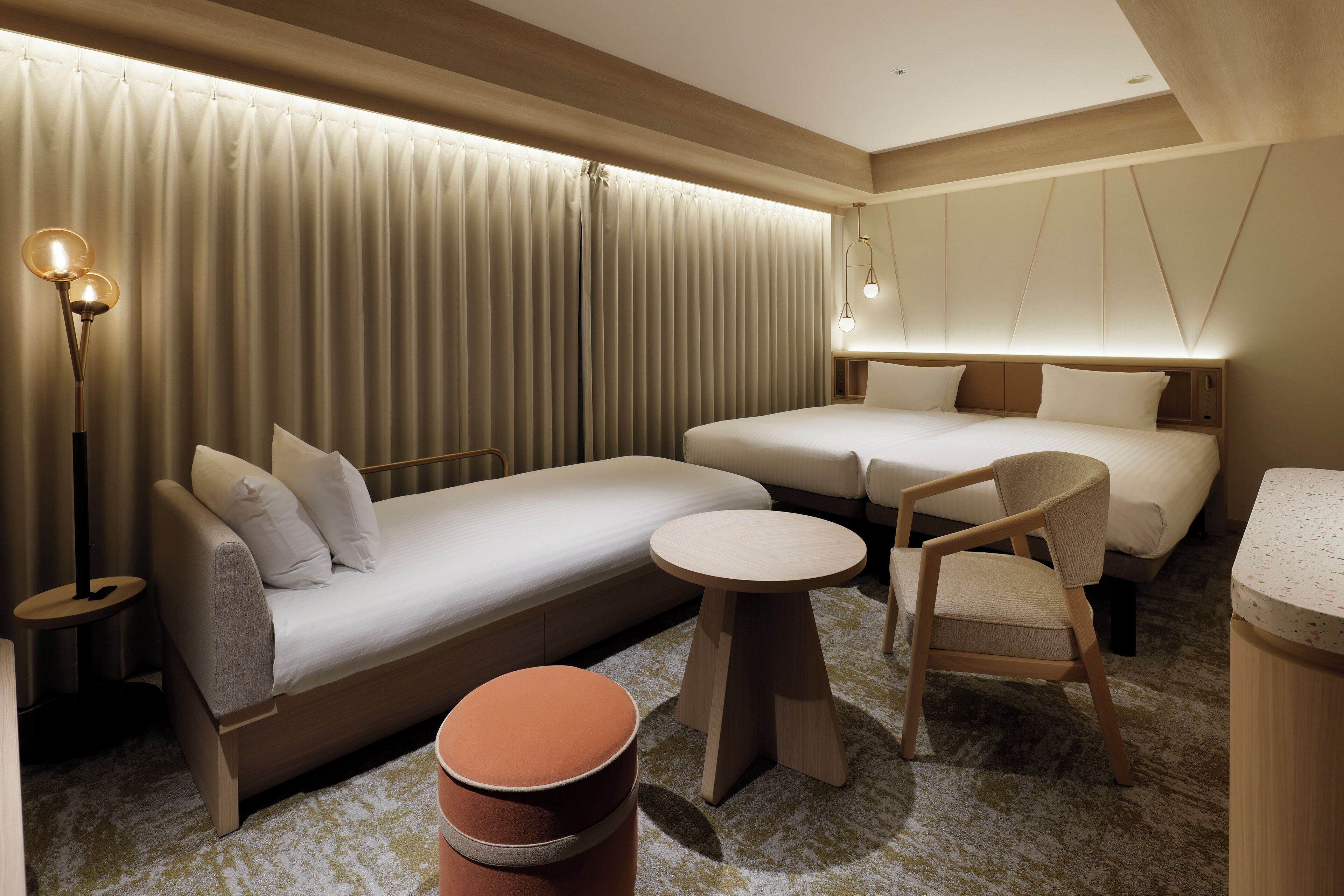 Ein Hotelzimmer mit einer Couch, zwei Betten, einem Sessel, einem kleinen Tisch und einer Lampe.