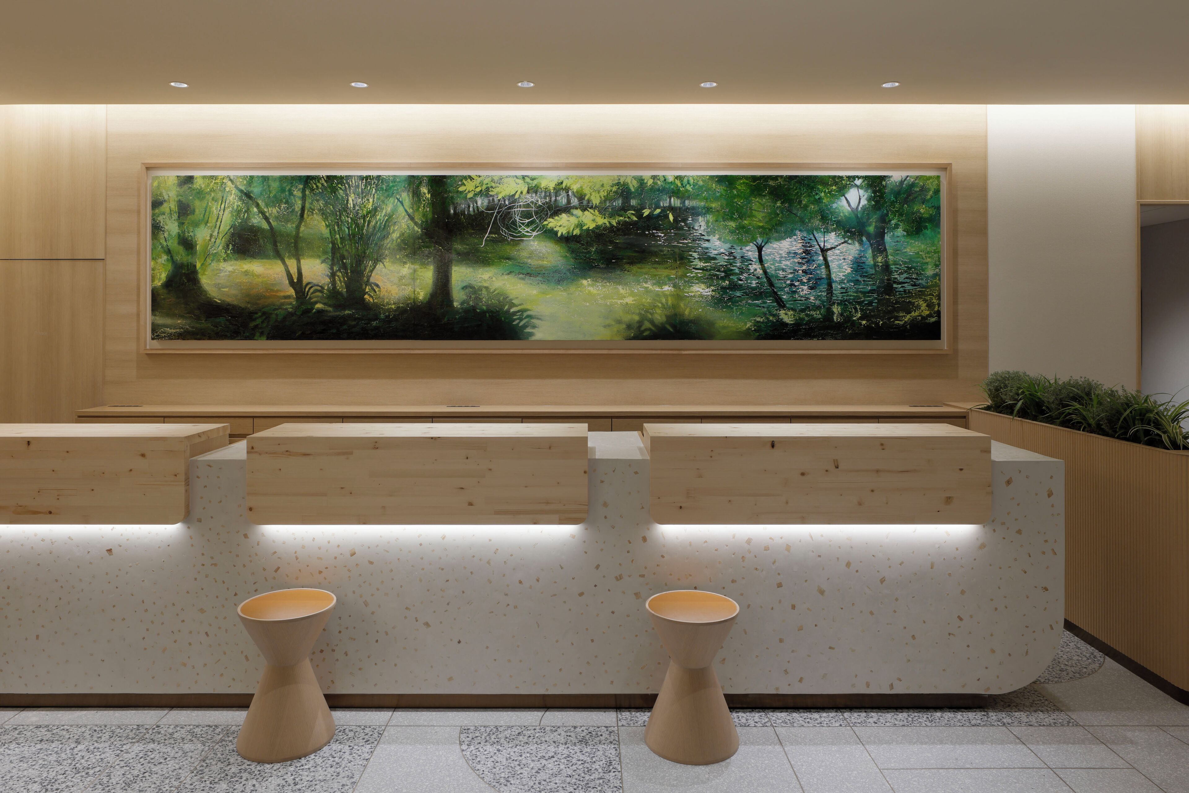 A reception area with a large painting of a forest, wooden reception desks, and two stools.