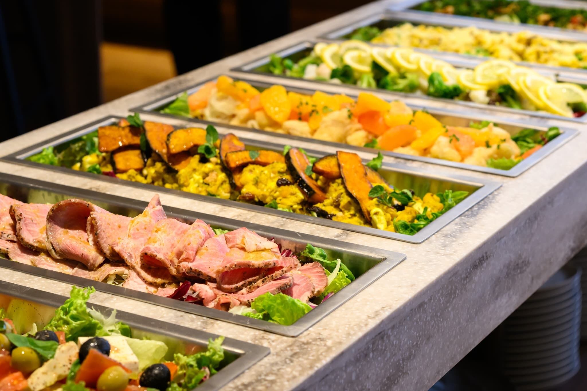Un buffet con diverse opzioni gastronomiche, tra cui carni, insalate e frutta.
