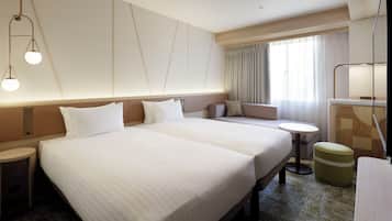 A hotel room with two large beds, a small sofa, a round table, and a green ottoman.