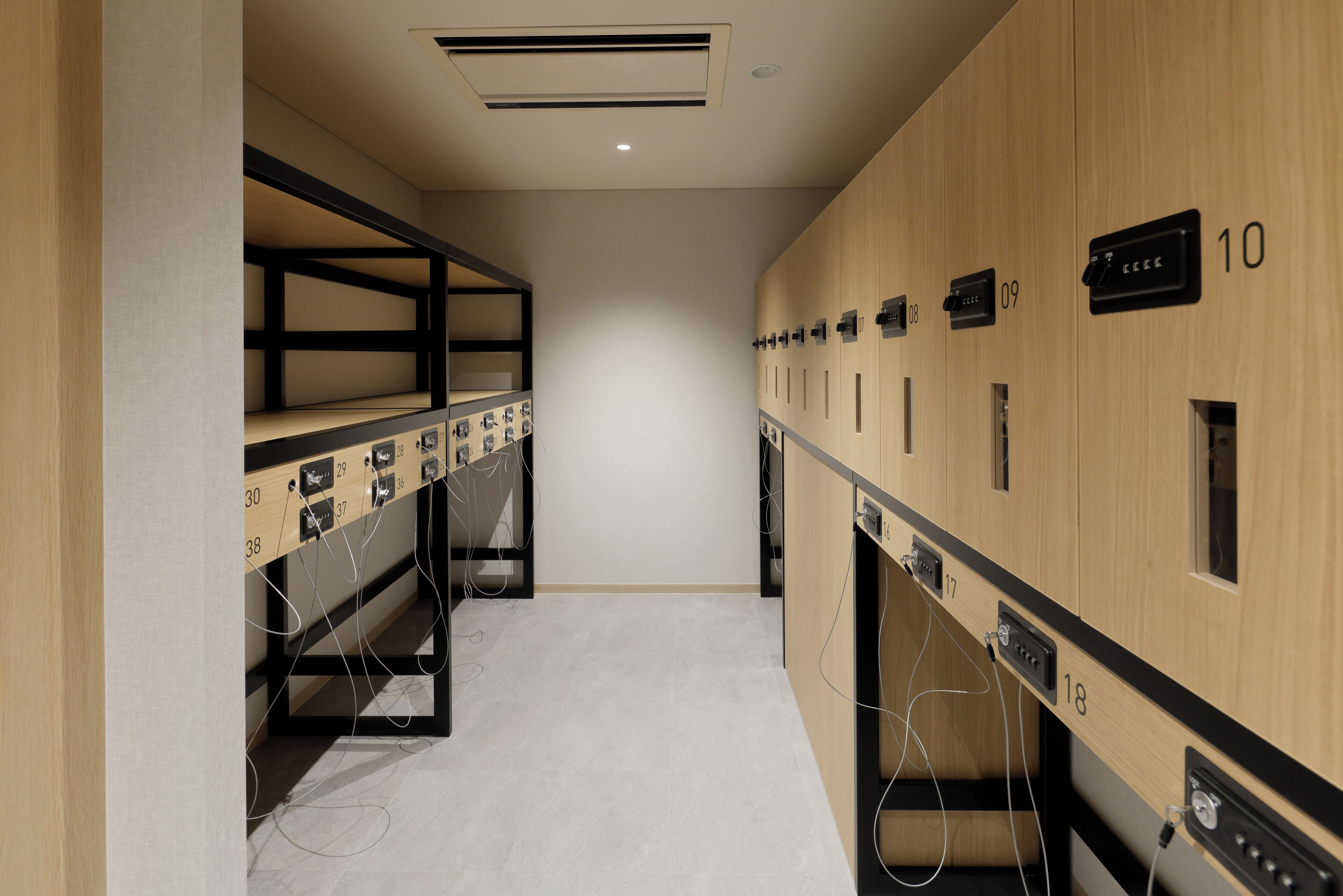 A hotel corridor with lockers numbered 10 to 38, a ceiling with ventilation, and a clean, tiled floor.