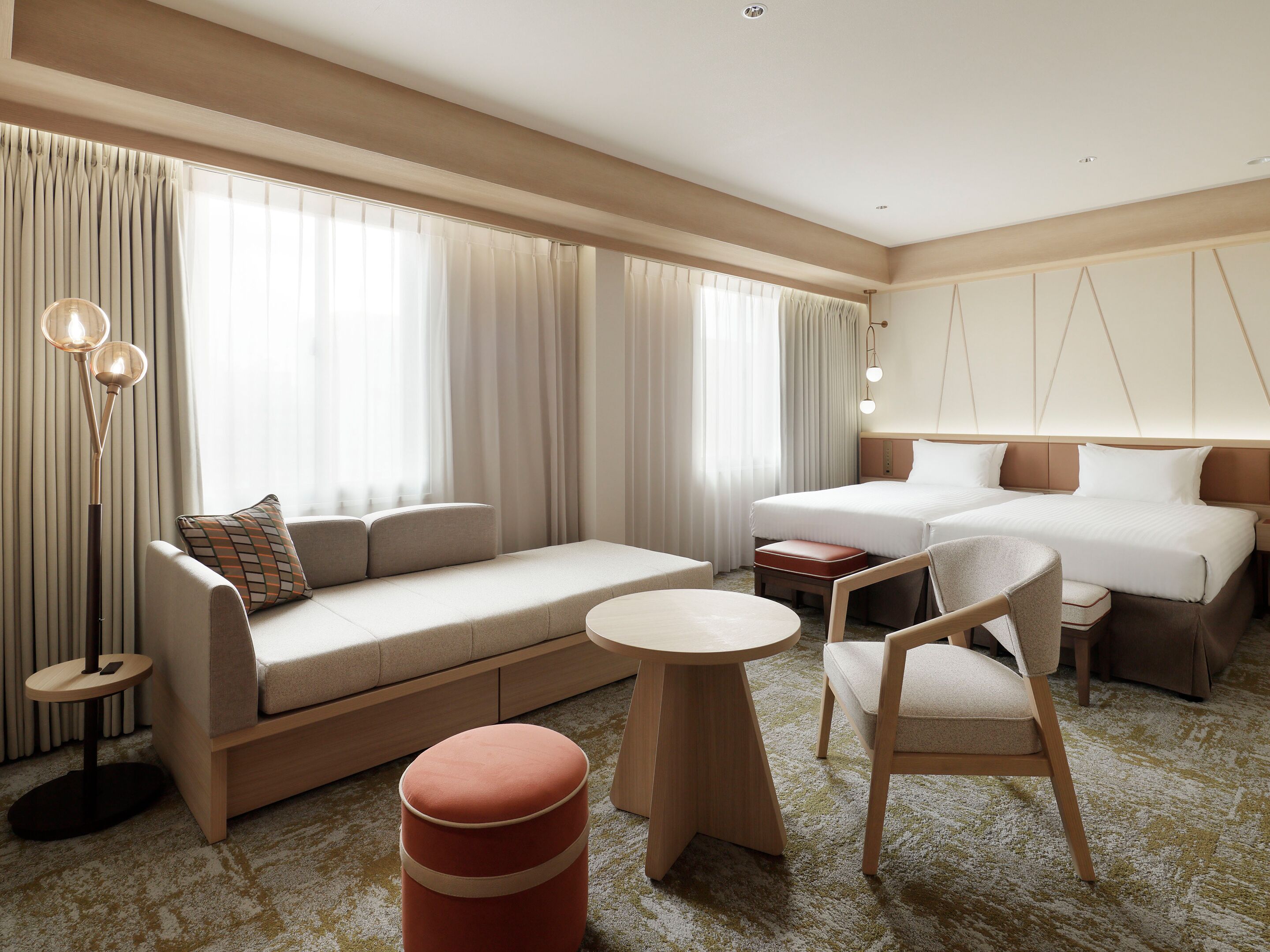 A modern hotel room with a sofa, two beds, a round table, and a chair.