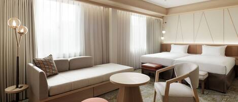 Una habitación de hotel moderna con sofá, dos camas, una mesa redonda y una silla.