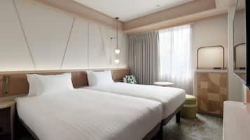 A hotel room with two beds, a bedside table, a round table, a mirror, and a window with curtains.