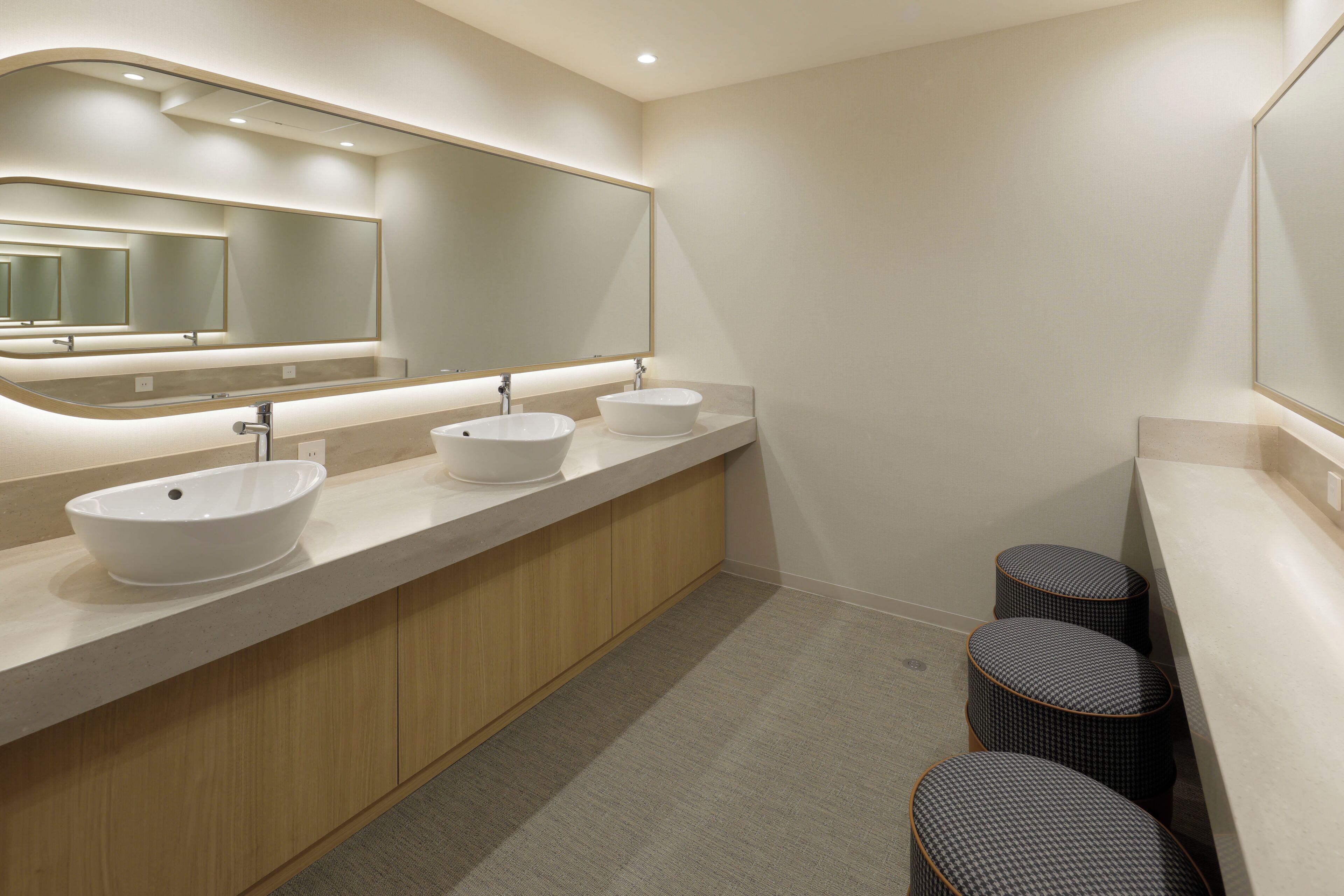 A modern bathroom with three sinks, a large mirror, and a wooden vanity.