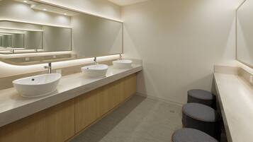 A modern bathroom with three sinks, a large mirror, and a wooden vanity.