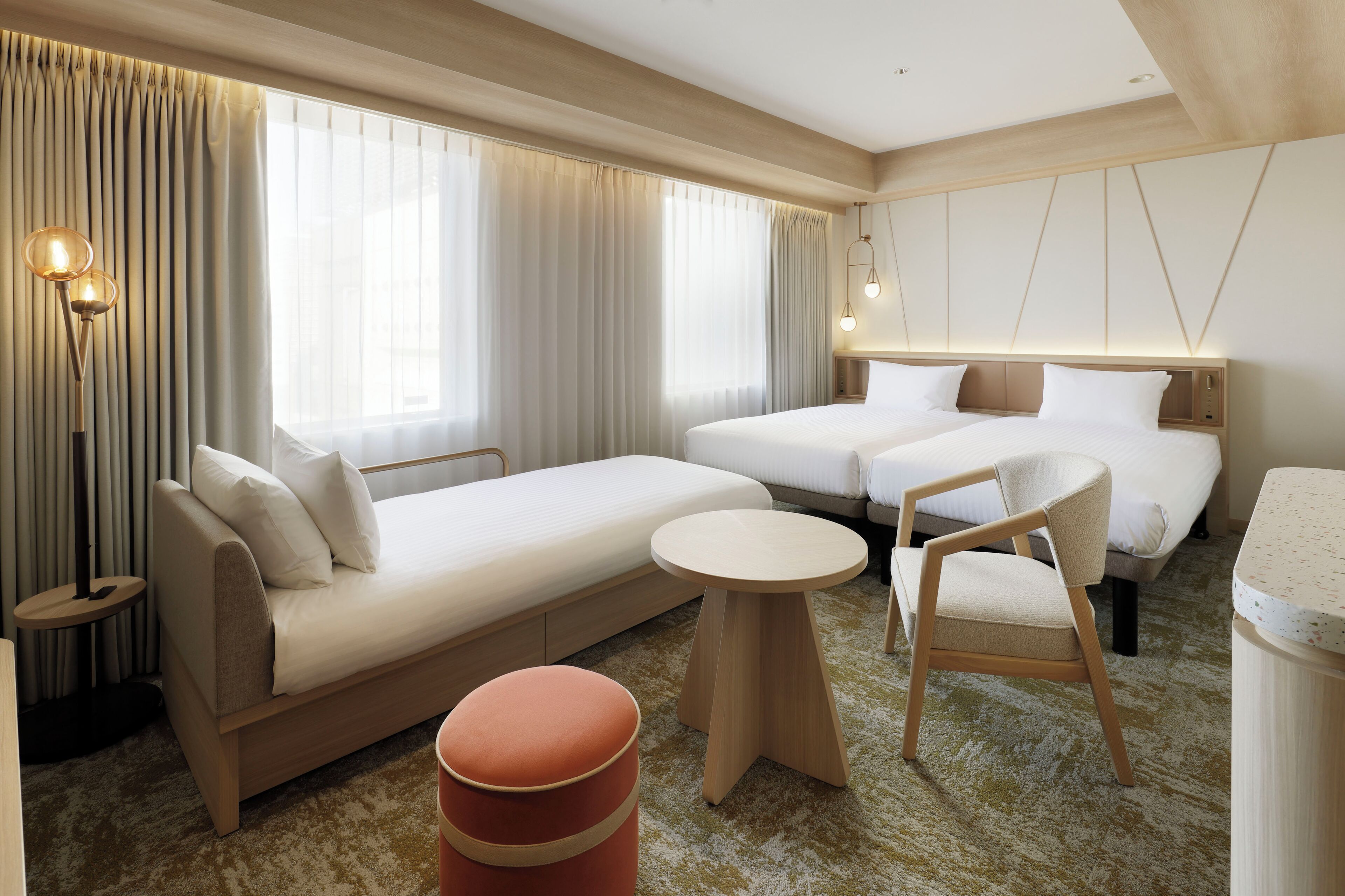A modern hotel room with a sofa, two single beds, a round table, a chair, and a small ottoman.