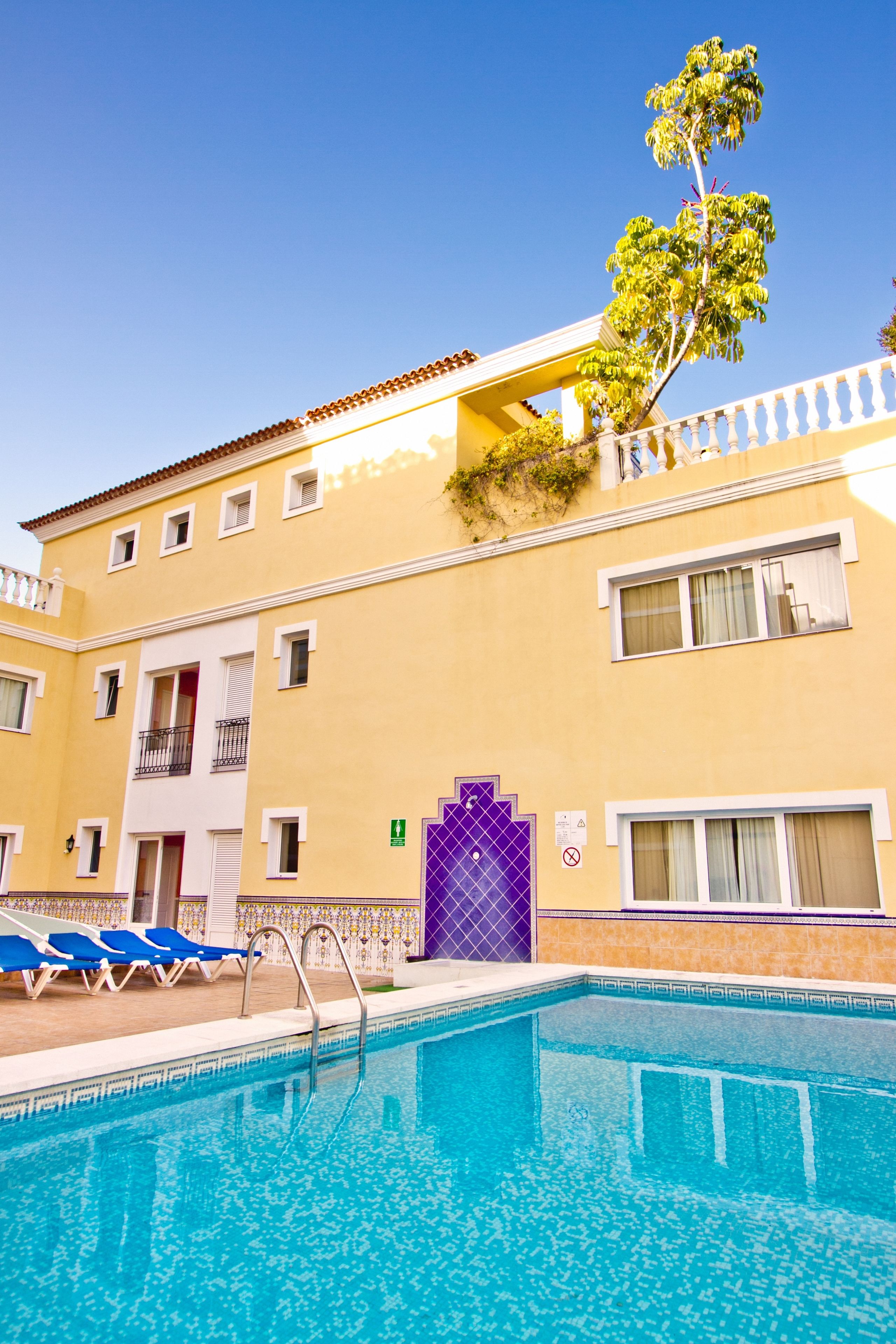 Un hôtel doté d’une piscine, d’une porte violette et d’un arbre qui pousse sur le balcon.