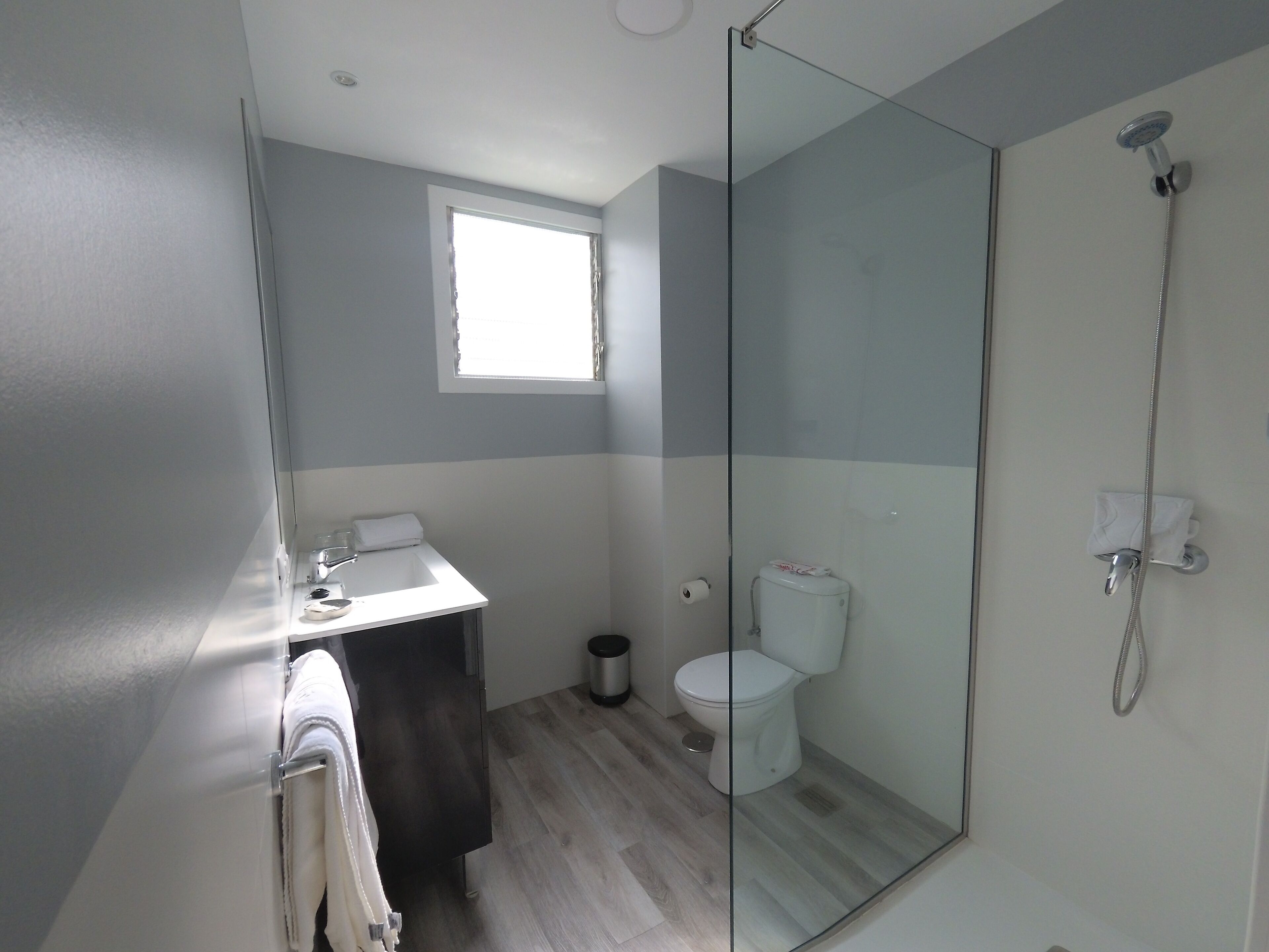 A modern bathroom with a glass shower enclosure, a toilet, and a sink with a towel.