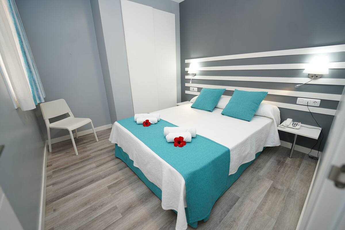 A modern hotel room with a large bed, a bedside table with a phone, and a chair.