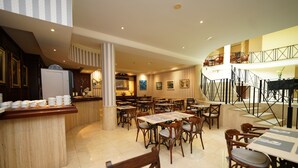 A spacious hotel dining area with multiple tables and chairs, a central column, and a kitchen area in the background. - RF Apartamentos Bambi - Adults Only (Puerto de la Cruz)