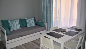 A room with a sofa bed, a dining table with four chairs, and a window with curtains. - RF Apartamentos Bambi - Adults Only (Puerto de la Cruz)