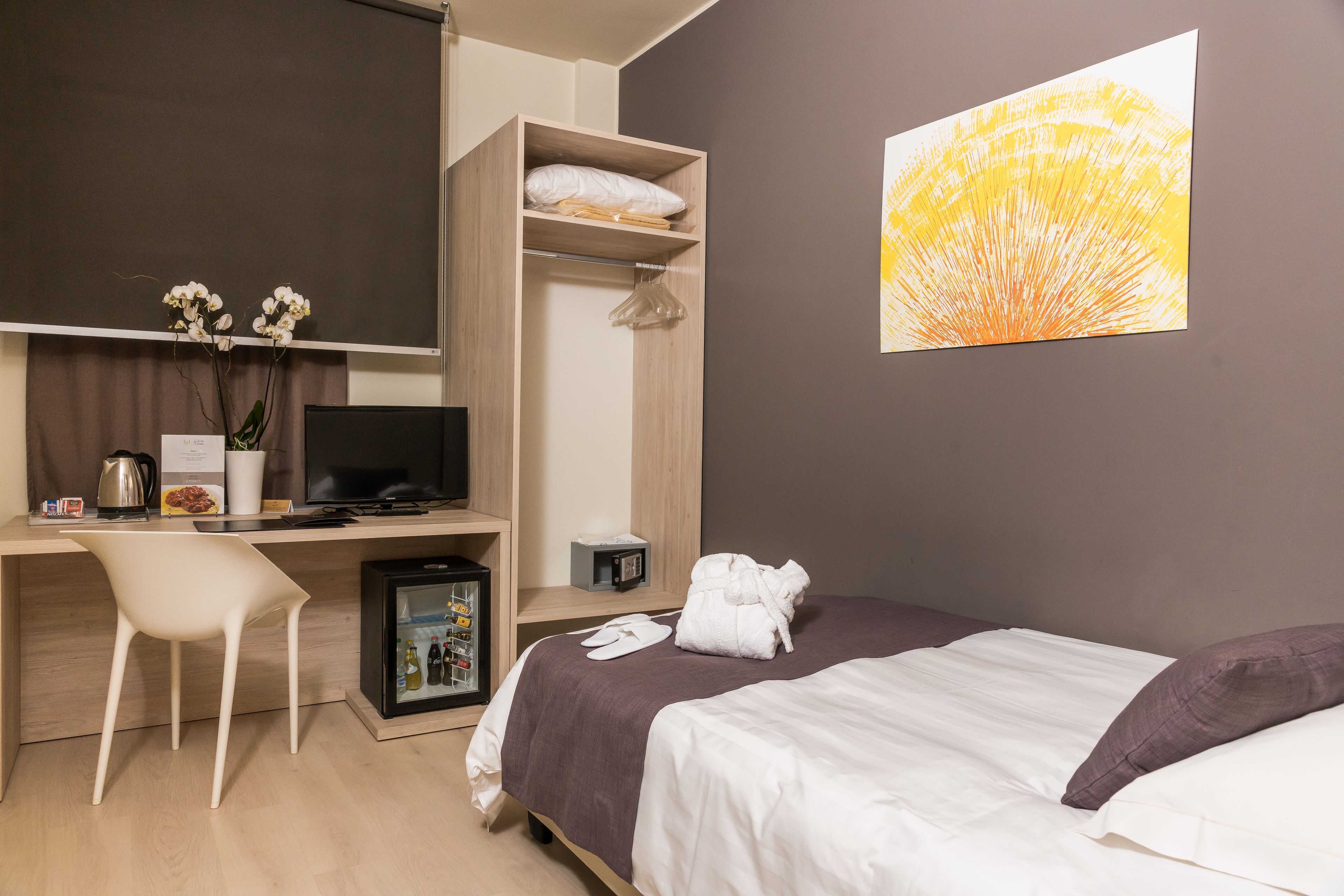 Une chambre d’hôtel équipée d’un lit, d’un bureau avec un ordinateur, d’une chaise, d’un petit réfrigérateur et d’un téléviseur fixé au mur.