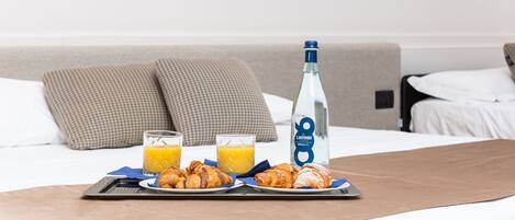 A neatly made breakfast tray on a bed with a bottle of water, two glasses of orange juice, and croissants.