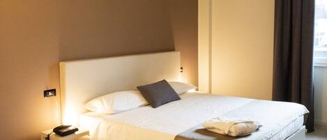 A hotel room with a large bed, bedside table with a phone, and a window with curtains.
