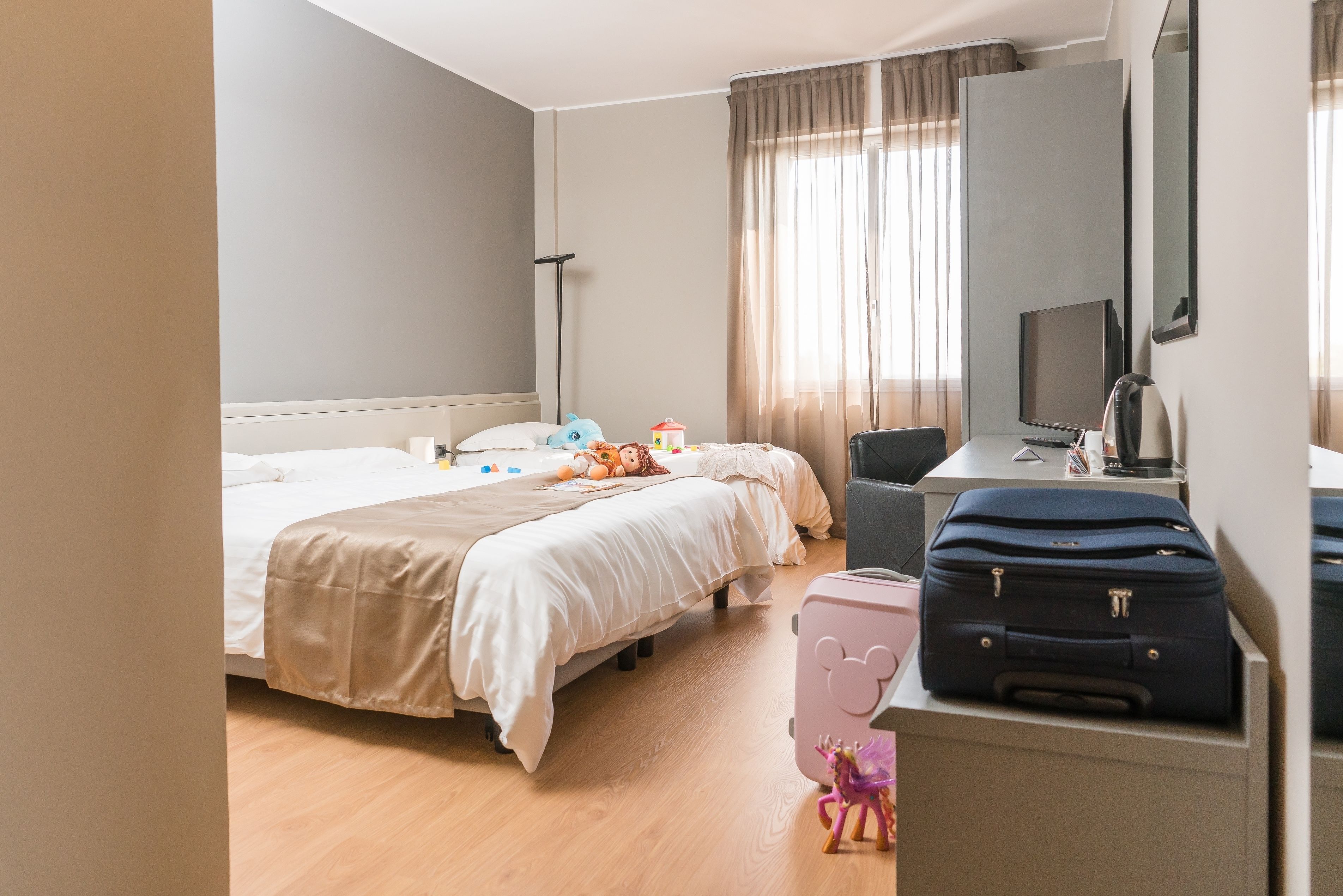 Habitación de hotel con cama, escritorio, silla, televisor y maleta.