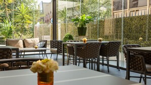 An outdoor dining area with tables and chairs, a potted plant, and a view of greenery and buildings. - Helios Hotel Monza (Monza)