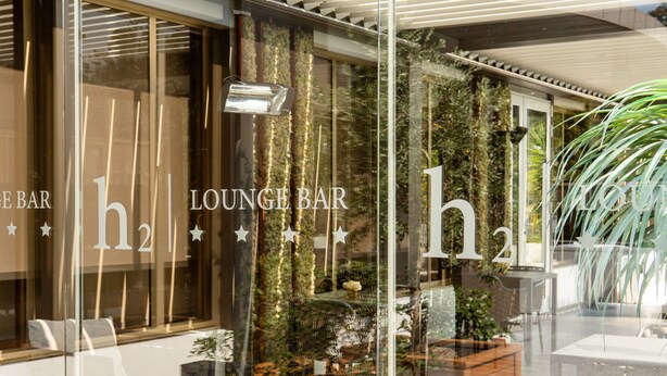 A lounge bar with a glass facade, indoor plants, and a wooden planter. - Helios Hotel Monza (Monza)