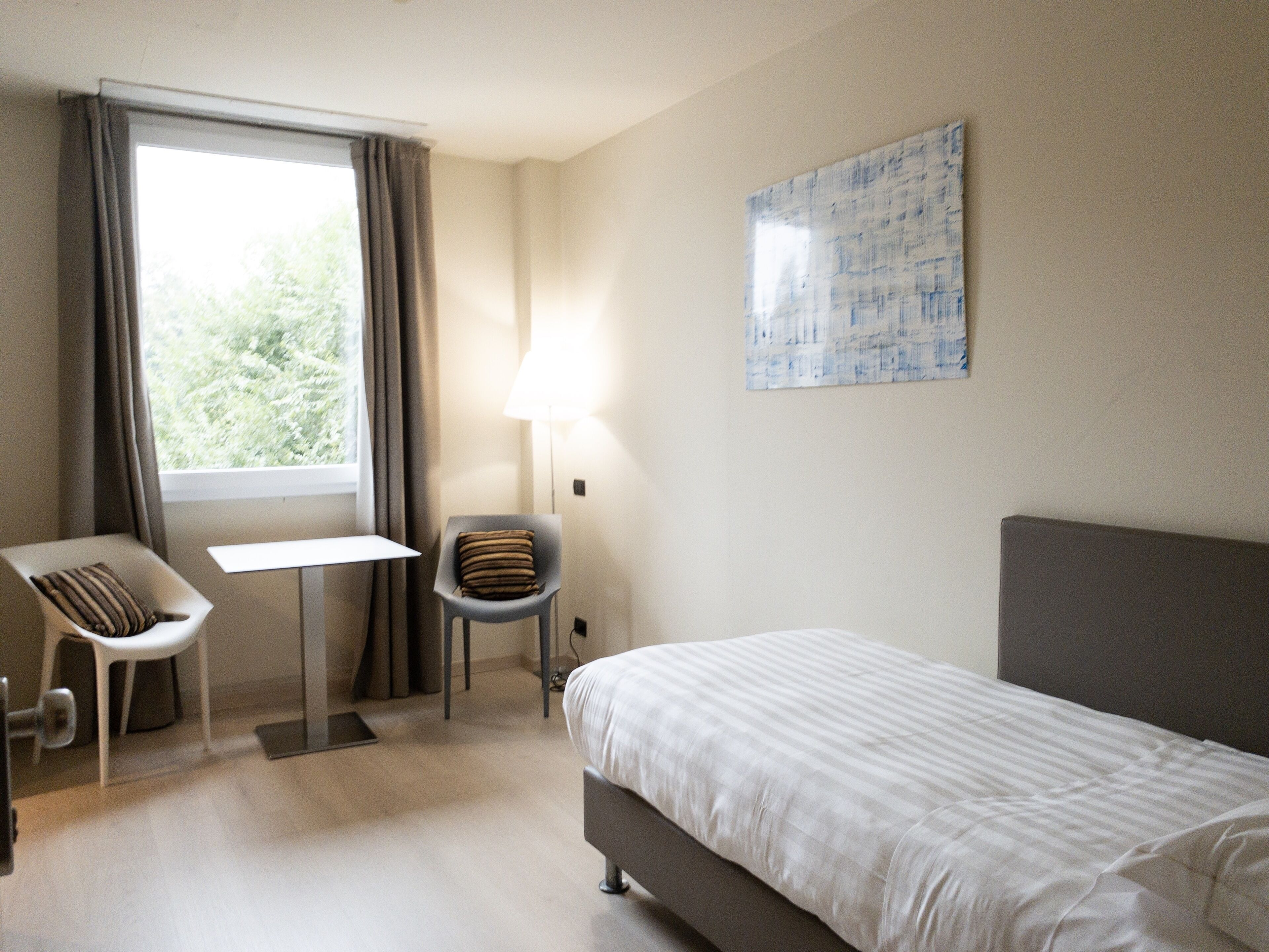 A hotel room with a bed, a desk, a chair, a lamp, and a window with curtains.