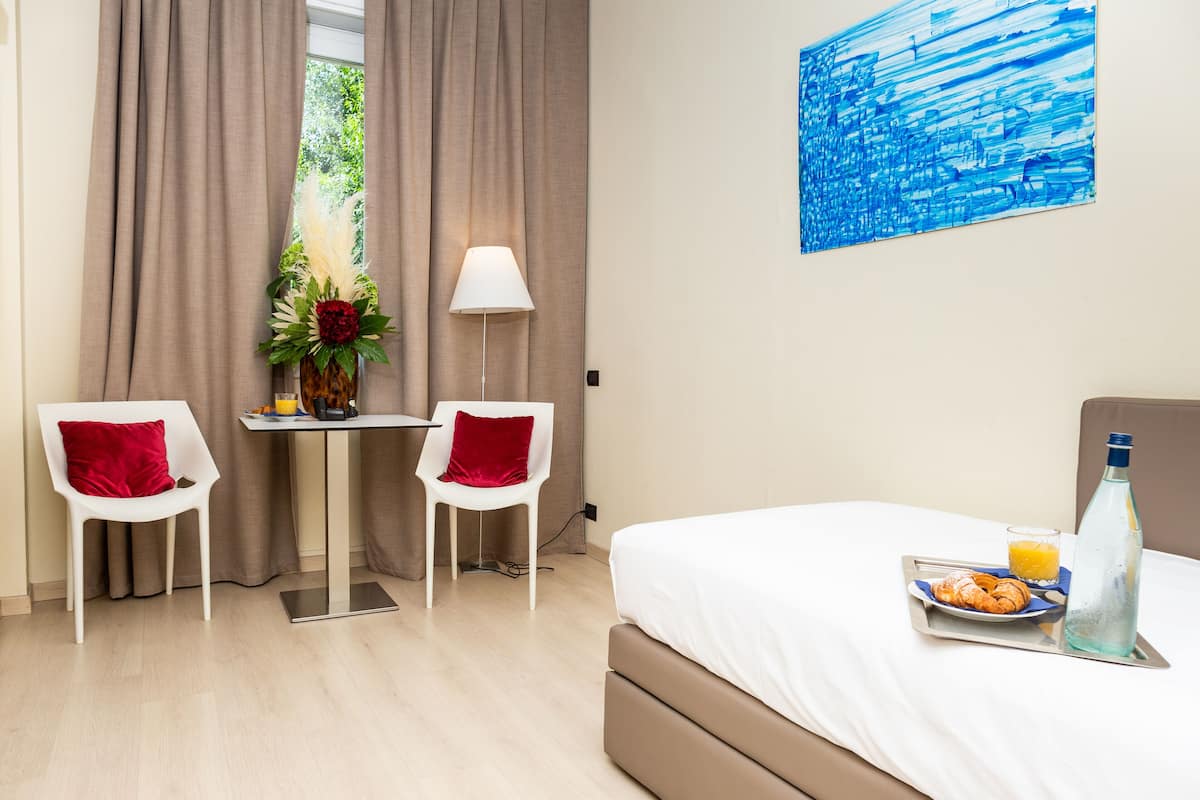Une chambre d’hôtel avec un lit, une table et des chaises, une lampe, un tableau et un plateau de petit-déjeuner avec des croissants et du jus de fruits.