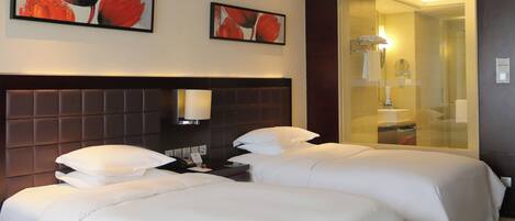 Habitación de hotel con dos camas, cabeceros, lámparas de noche y dos cuadros enmarcados con motivos florales en la pared.